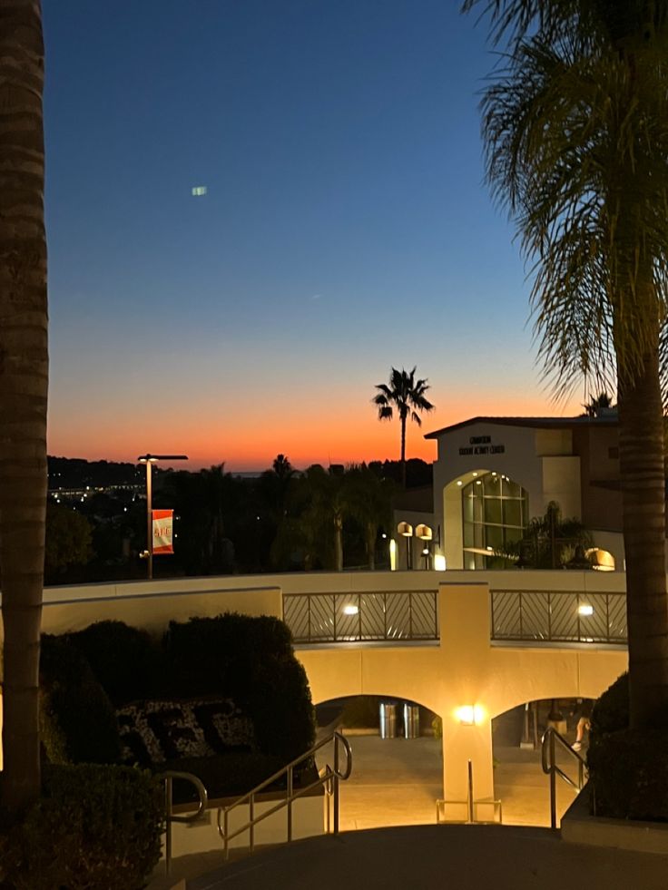 the sun is setting behind palm trees in front of a building with stairs and balconies