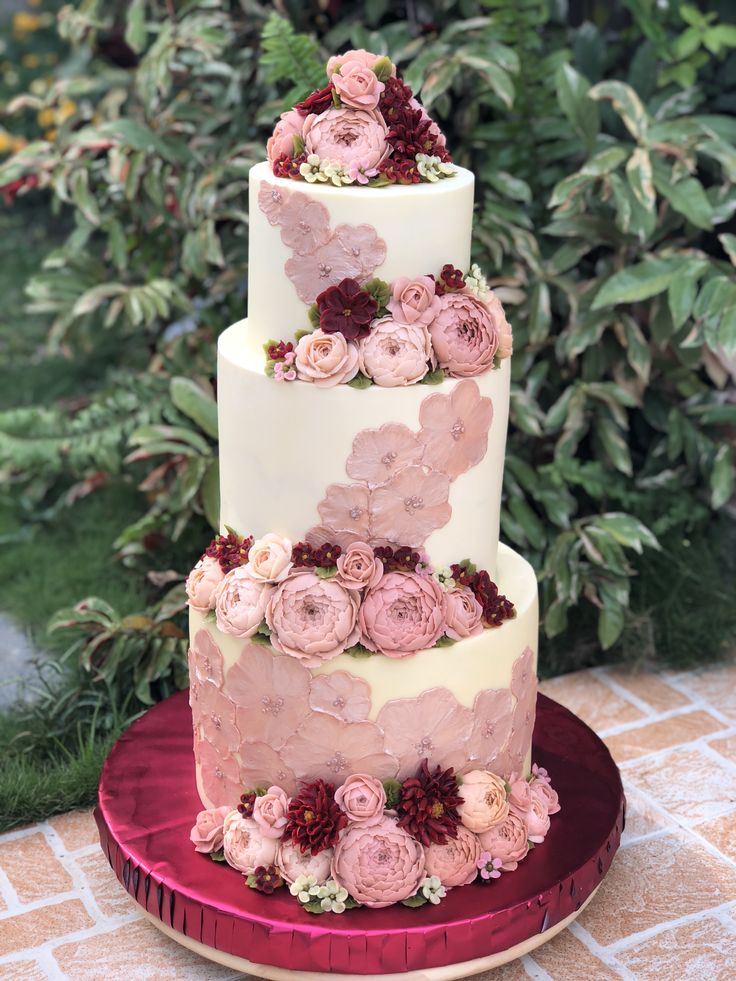 a three tiered wedding cake with pink flowers on the top and bottom, sitting on a red platter