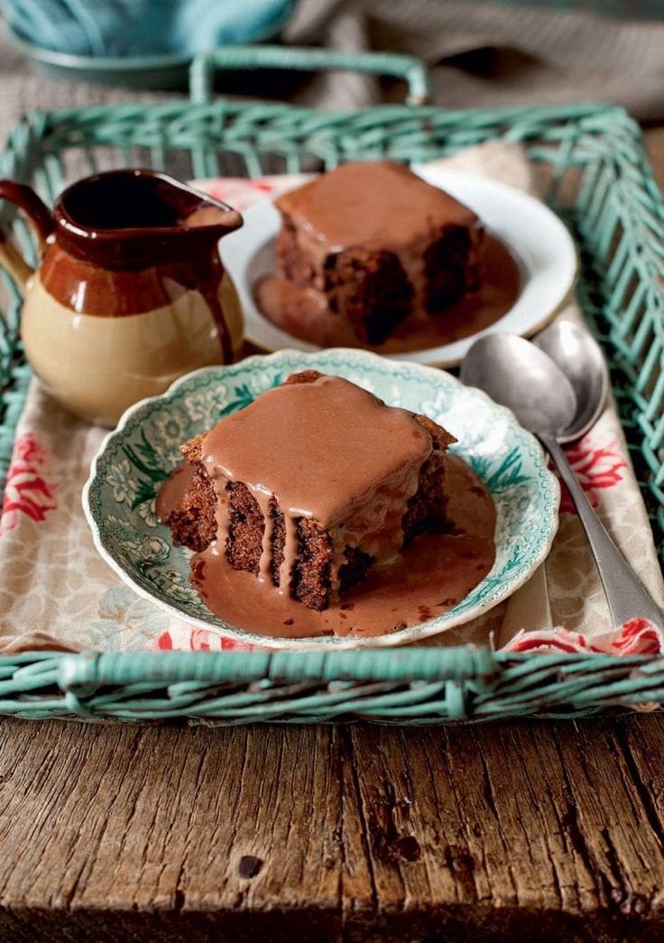 two pieces of chocolate cake on a plate with a teapot and spoon in the background