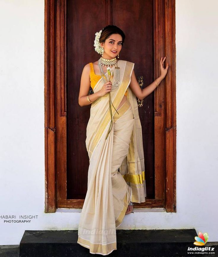 a woman standing in front of a wooden door wearing a white and yellow sari