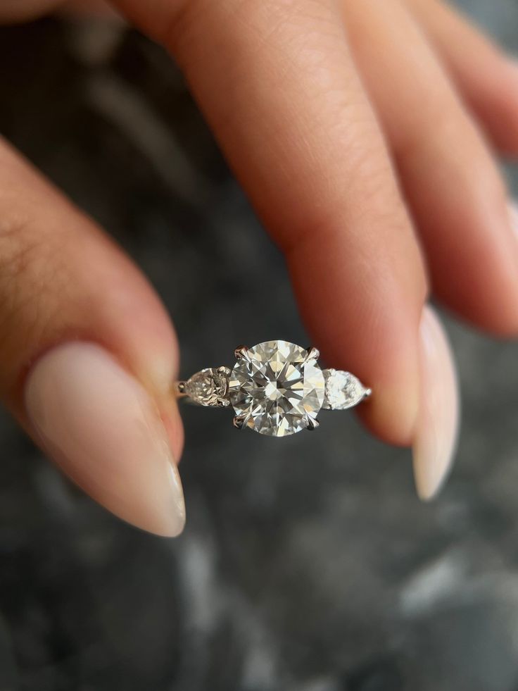 a woman's hand holding an engagement ring with three diamonds on it and the middle finger