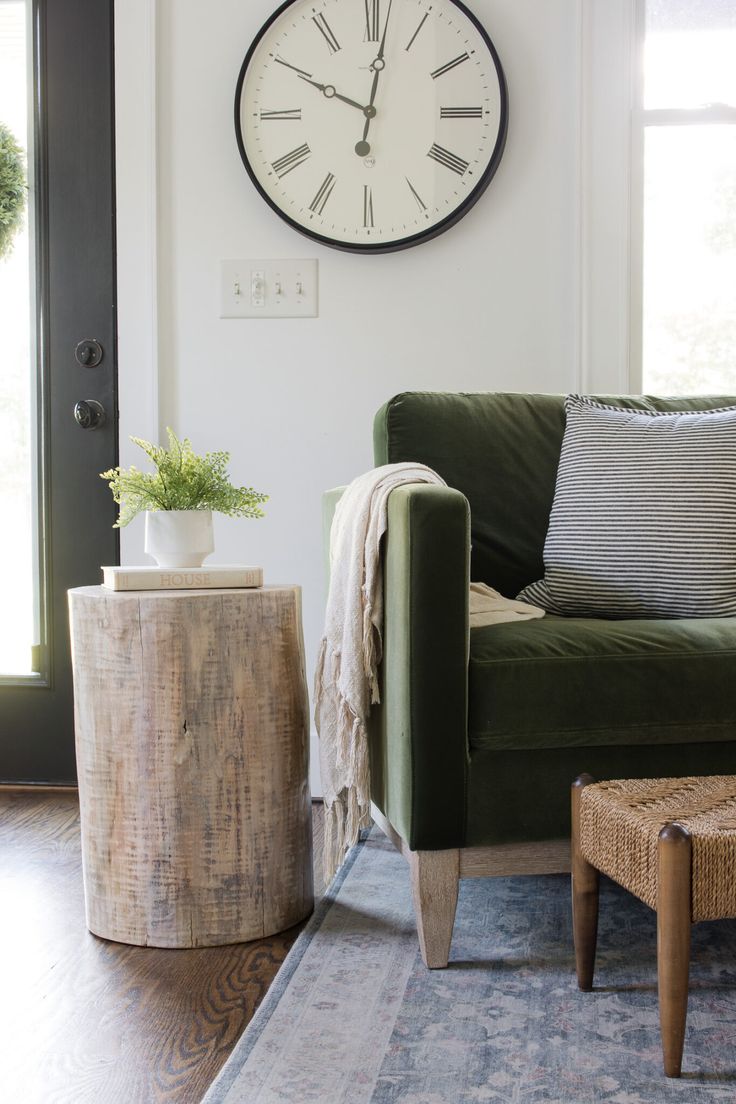 a living room with a green couch and large clock on the wall above it's door