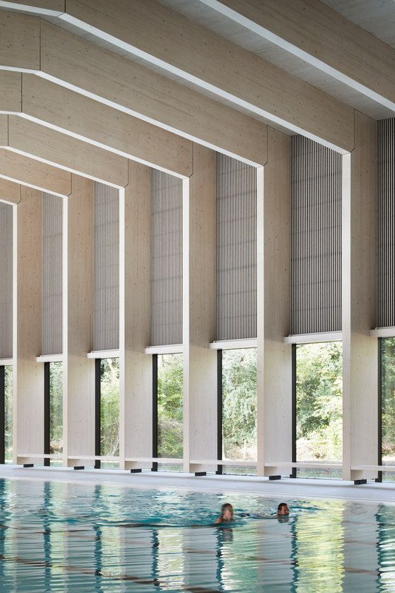 an indoor swimming pool with several people in the water and blinds on the windows above it