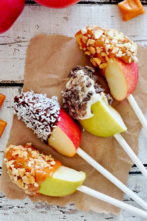 four apples on sticks with nuts and caramel are sitting on a piece of brown paper