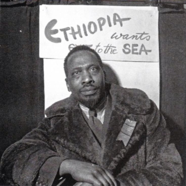 a black and white photo of a man sitting in front of a sign that says ethiopian atlantic to the sea