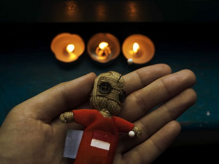 a hand holding a small doll with candles in the background