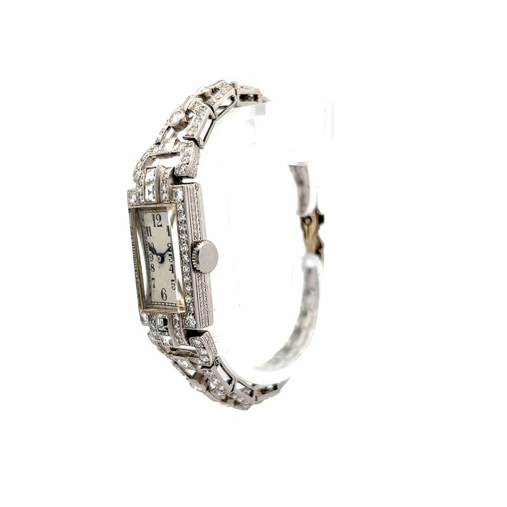 This antique Art Deco manual wind diamond watch, made from polished 14 karat white gold, features .60 carats of asscher cut diamonds with VS1 clarity and H color grade. Surrounding it are accent diamonds in various cuts, including old European, baguette, and single cuts, all bezel or channel set. These diamonds, ranging in size from 2.75 mm to 2.15 mm, contribute an additional .35 carats. The watch also showcases intricate milgrain detailing and engraving on the case, along with tapered links for added comfort. This vintage-inspired timepiece combines functionality with a rich sense of history. Classic Diamond White Watch With Brilliant Cut, Classic Platinum Diamond Watch With Brilliant Cut, Classic Wedding Jewelry And Watches With Diamond Hour Markers, Classic Round Diamond Watch With Accents, Classic Diamond Jewelry With Brilliant Cut, Classic White Gold Jewelry With Brilliant Cut, Classic Diamond White Watch For Anniversary, Art Deco Rectangular Watch With Diamond Hour Markers, Art Deco Rectangular Watch With Diamond Markers