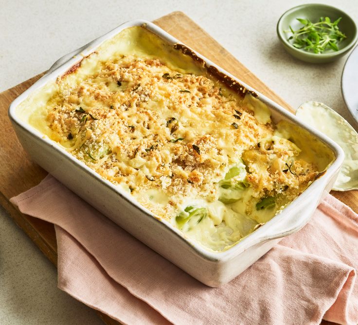 a casserole dish with cheese and broccoli in it on a cutting board