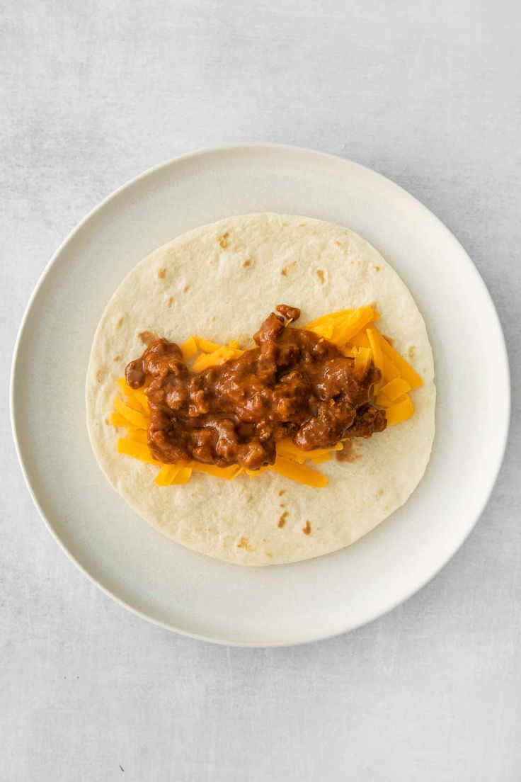 a tortilla topped with meat and cheese on a white plate