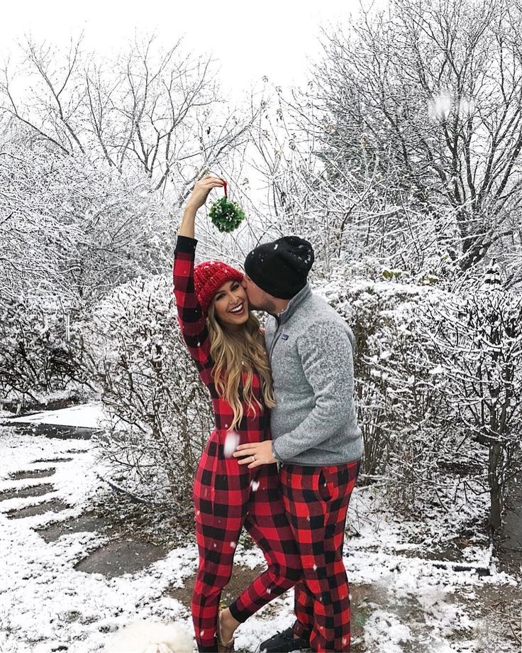 a man and woman dressed in plaid pajamas are standing on snow covered ground with their arms around each other