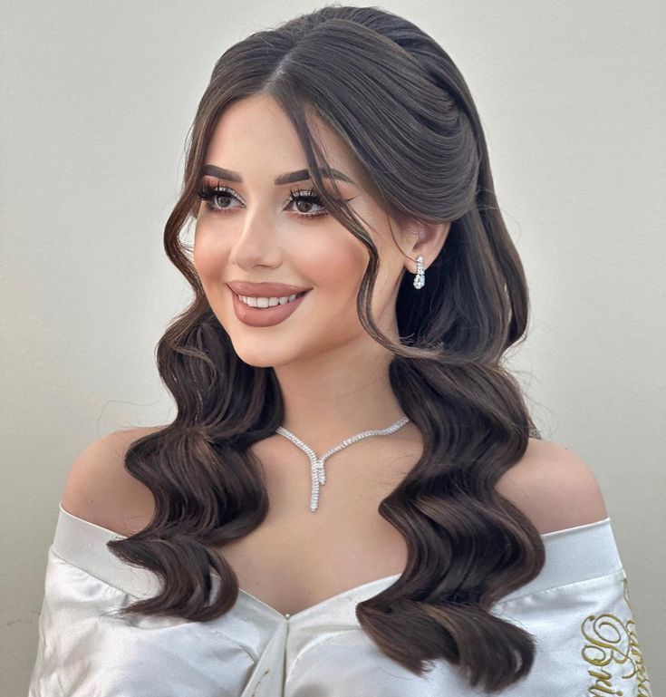 a woman with long dark hair wearing a white dress and diamond necklace, smiling at the camera