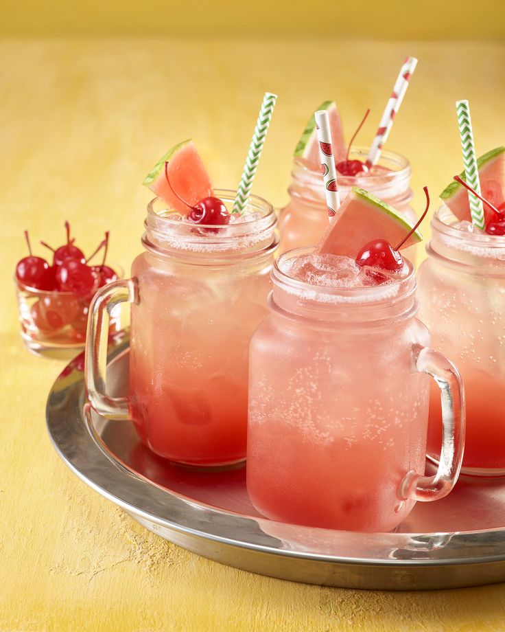 three mason jars filled with watermelon and garnished with cherries on a metal tray