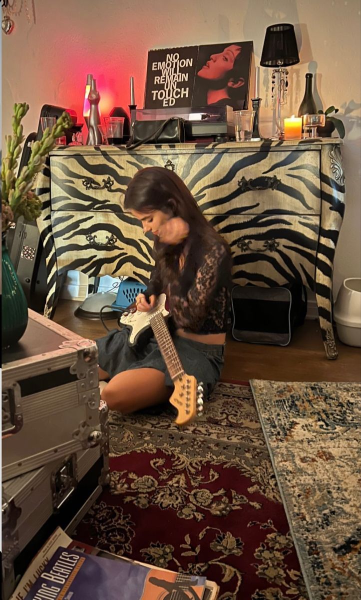 a woman sitting on the floor playing an electric guitar in front of a zebra print wall