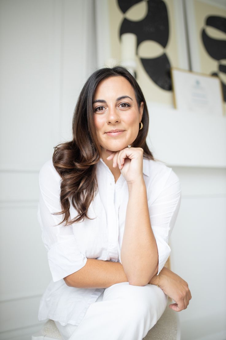 a woman sitting on top of a white chair in front of a wall with paintings