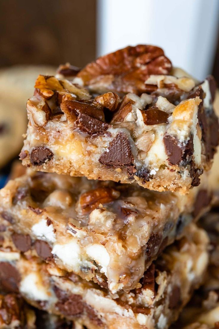 chocolate chip cookie bars stacked on top of each other with pecans in the background