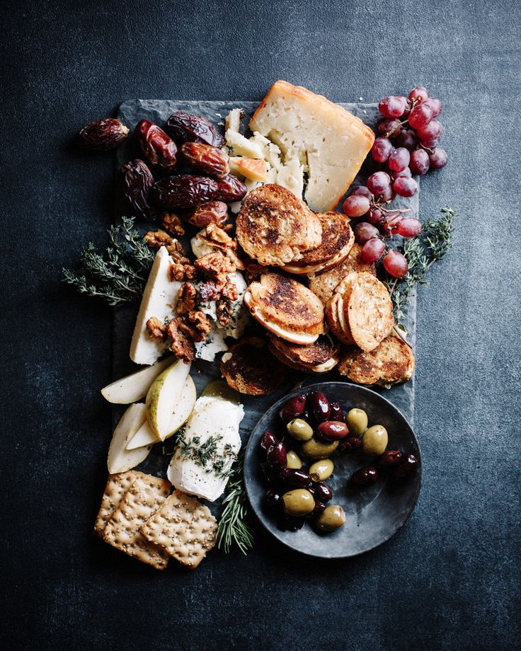 an assortment of cheeses, crackers and grapes on a platter with rosemary