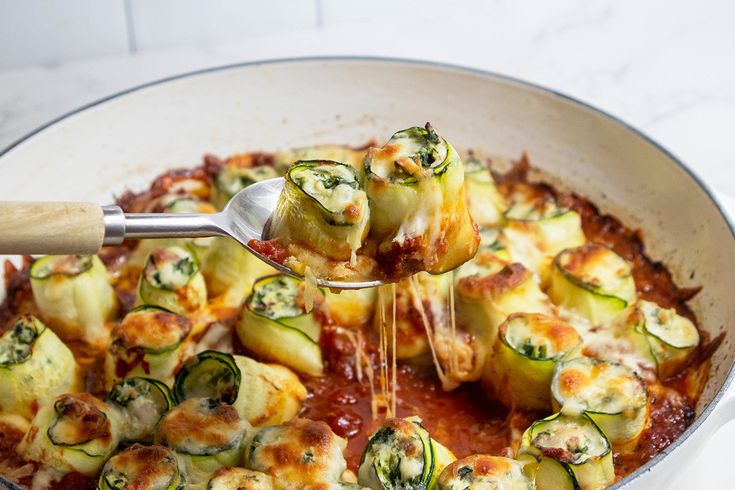 a pan filled with zucchini and sauce being spooned into the casserole