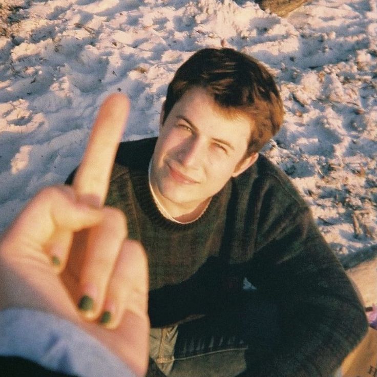 a young man sitting in the snow pointing at someone with his finger to the camera