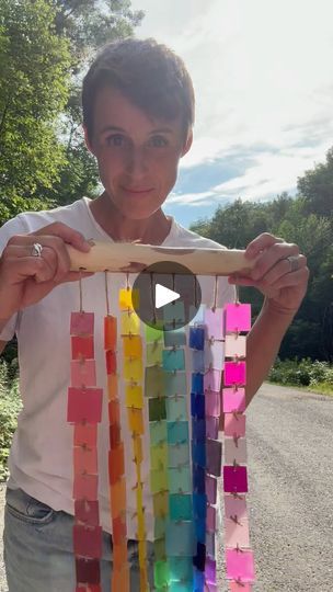 a woman is holding up a rainbow colored piece of wood that she made out of strips of paper