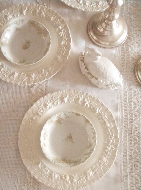 the table is set with white dishes and silver candlesticks on top of it