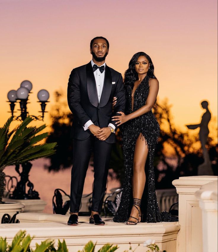 a man and woman standing next to each other in front of the sun setting behind them