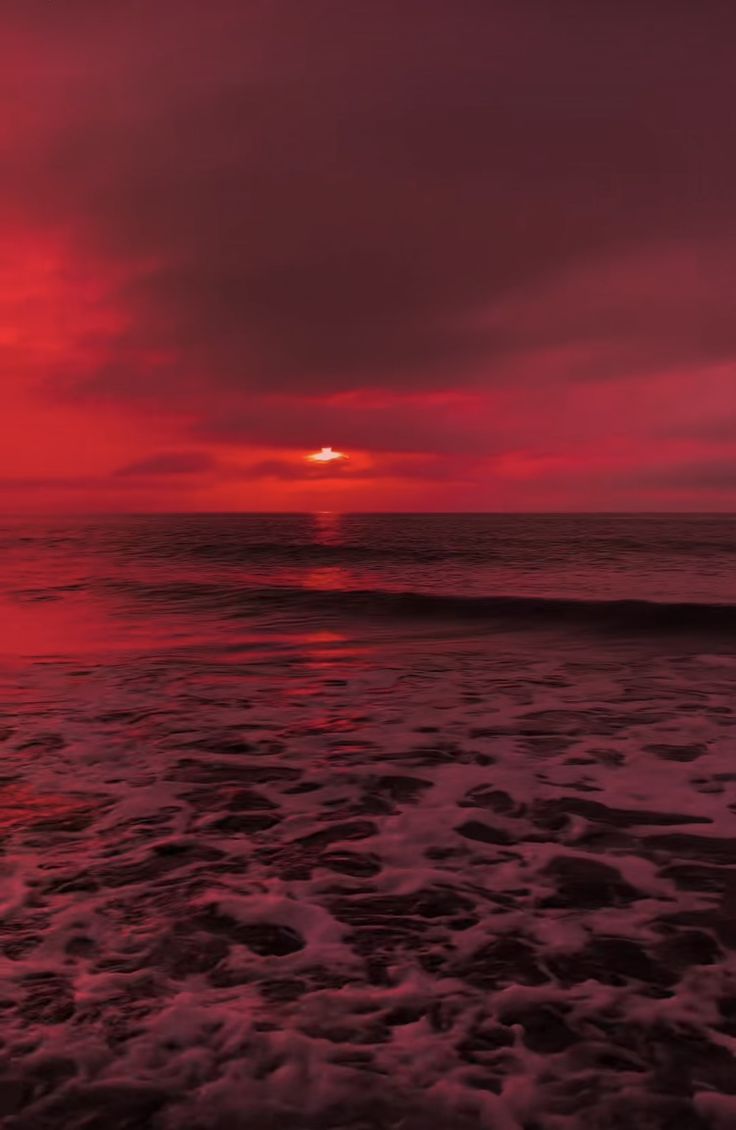 the sun is setting over the ocean with waves coming in to shore and red clouds