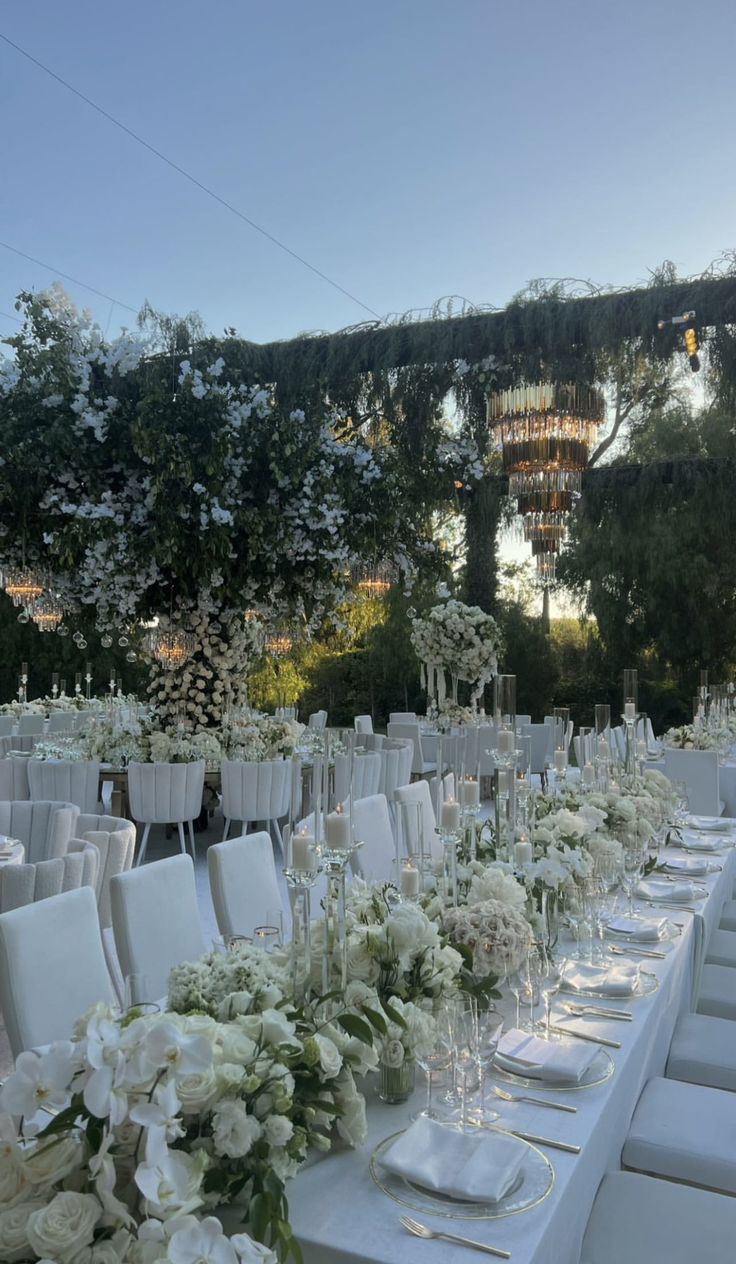 the tables are set with white flowers and place settings for an outdoor wedding reception at sunset