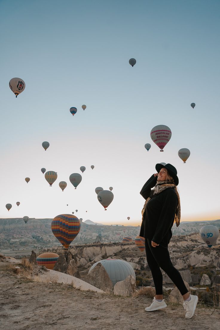 a woman standing on top of a hill next to hot air balloons in the sky