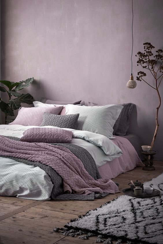 a bed with pink and grey sheets in a bedroom next to a plant on the floor