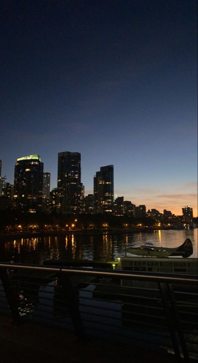 the city skyline is lit up at night with boats in the water and lights on