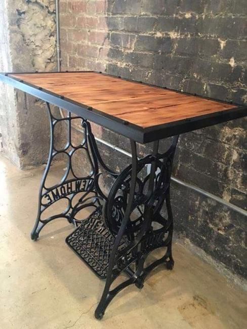 an old sewing machine table with a wooden top and black iron legs, against a brick wall