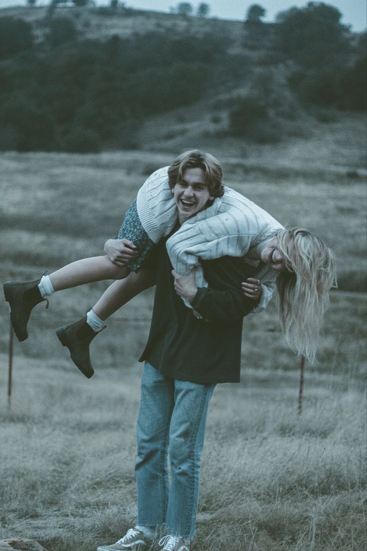 a man carrying a woman on his back in the middle of a field with trees