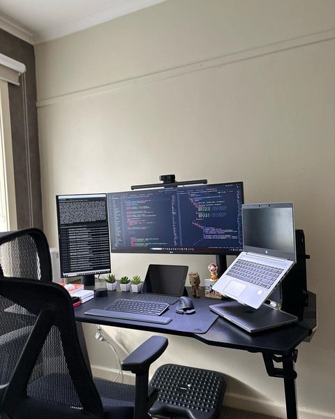 a desk with two computer monitors and a laptop on it in front of a window