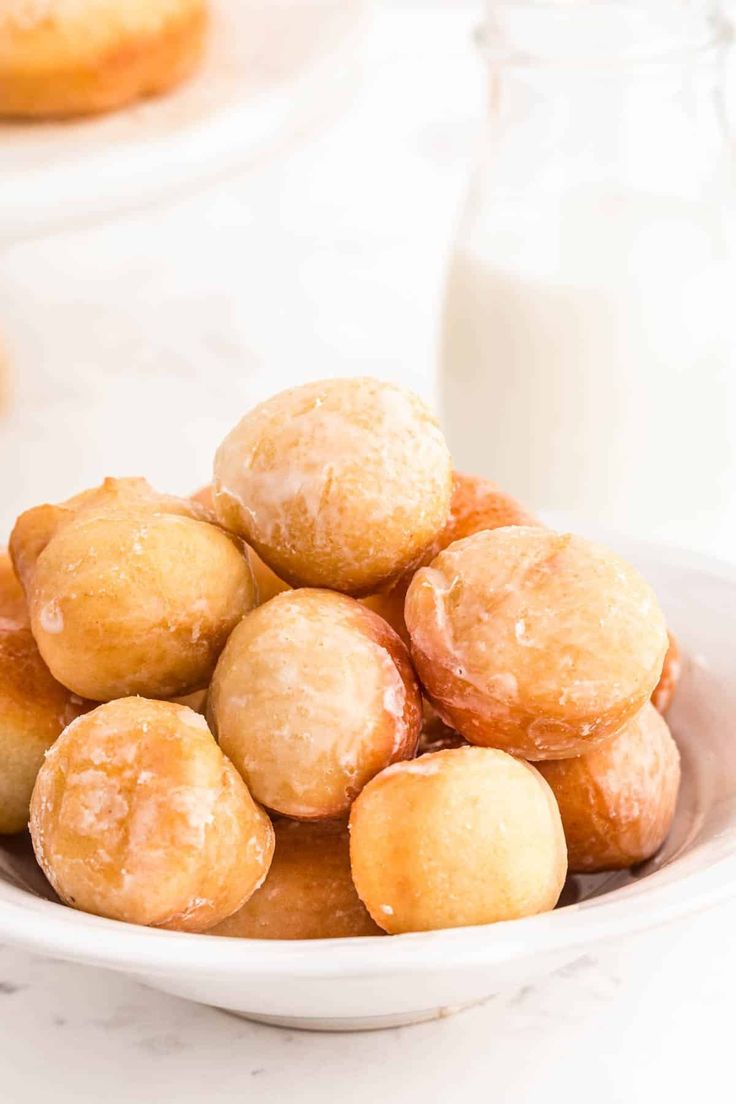 a white bowl filled with doughnuts next to a glass of milk on a table