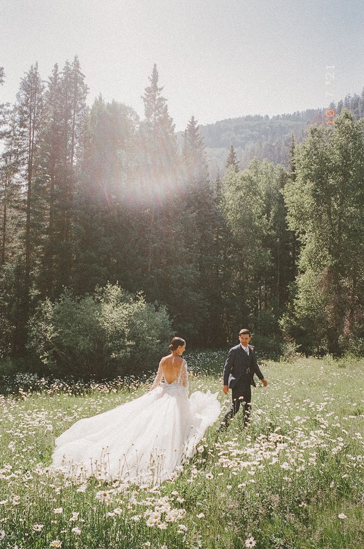 a bride and groom walking through a field with wildflowers in the foreground