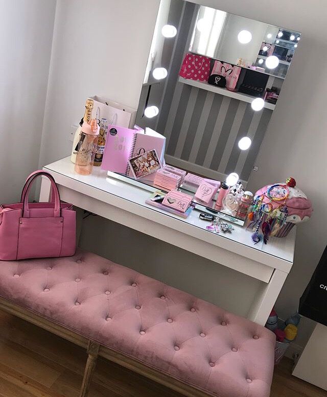 a pink bench sitting in front of a mirror next to a table with a purse on it