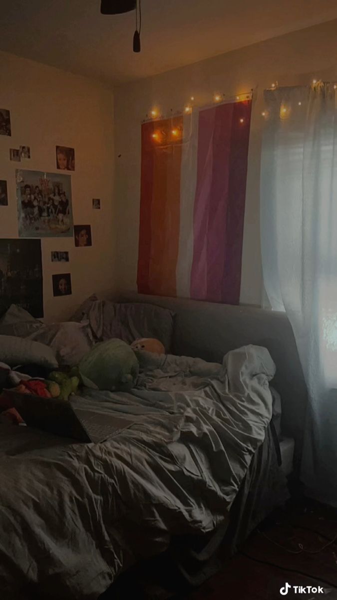 a person laying on a bed in front of a window with curtains and lights hanging from the ceiling