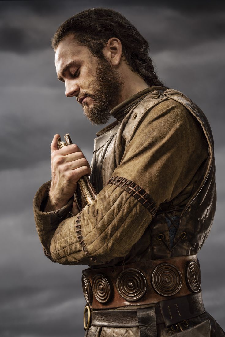 a man with long hair and beard standing in front of a cloudy sky holding a cell phone