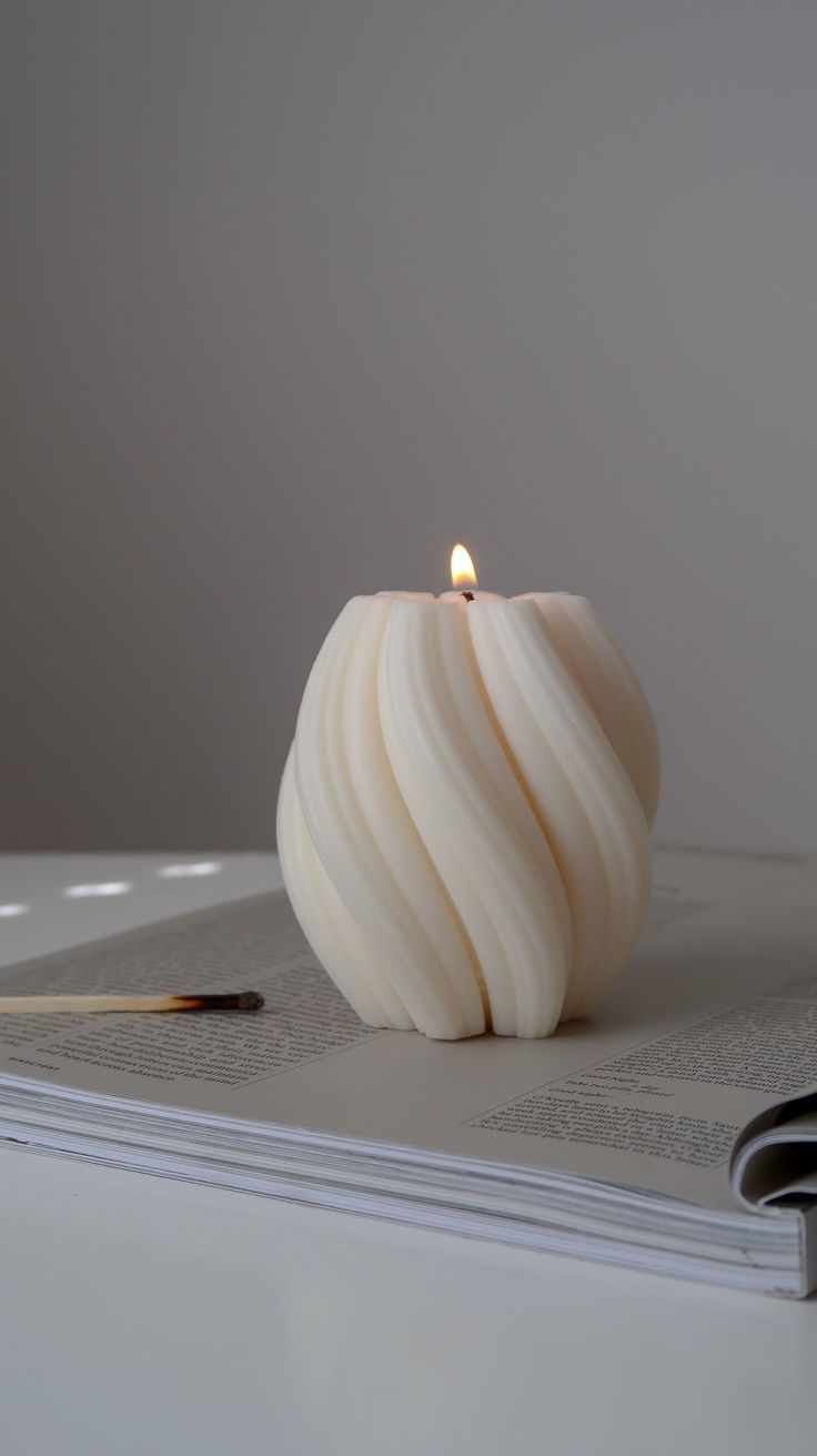 a white candle sitting on top of an open book next to a pen and pencil