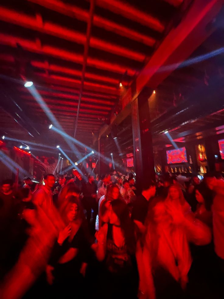 a group of people dancing at a party with red and blue lights on the ceiling