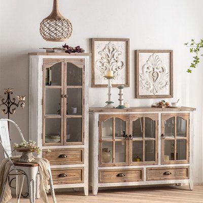 a white and wooden cabinet sitting in a living room next to a chair with a vase on top of it