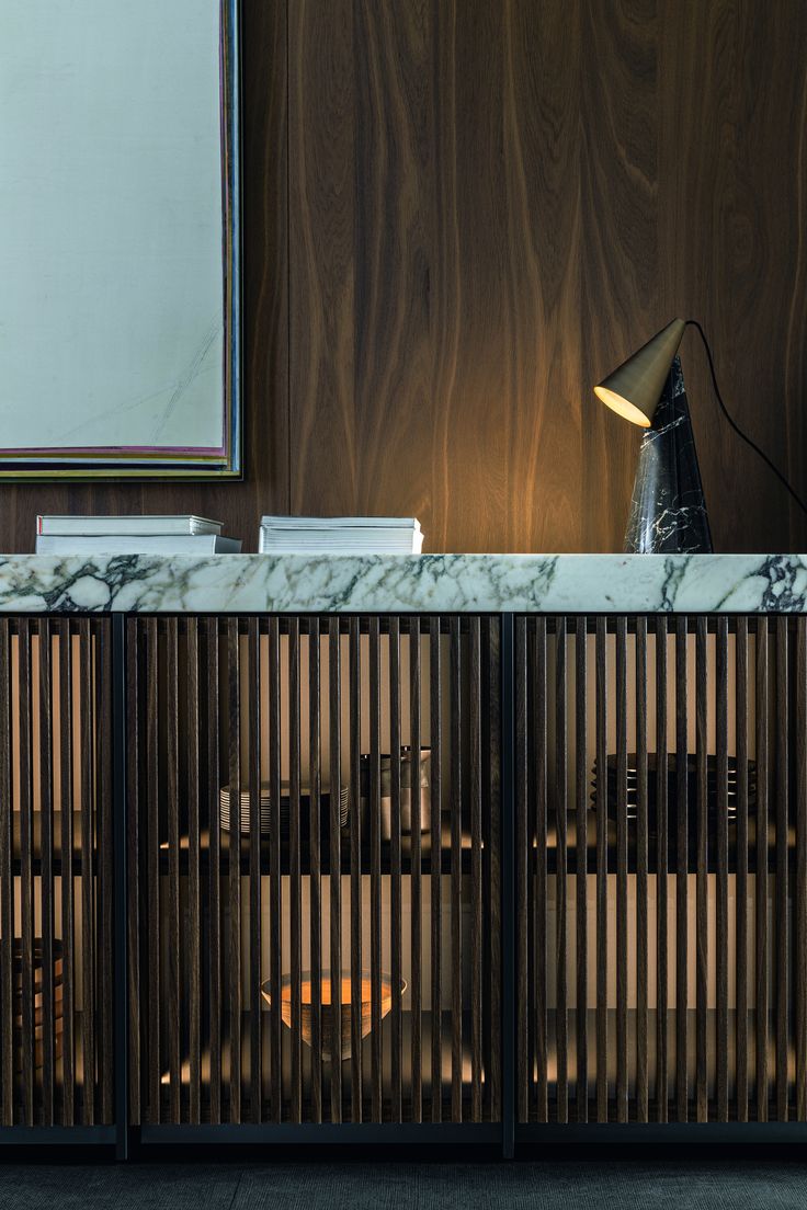 a marble top sideboard with wooden slats in front of a mirror and lamp