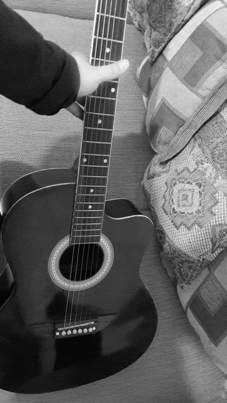 a black and white photo of someone playing an acoustic guitar on a couch with a pillow in the background