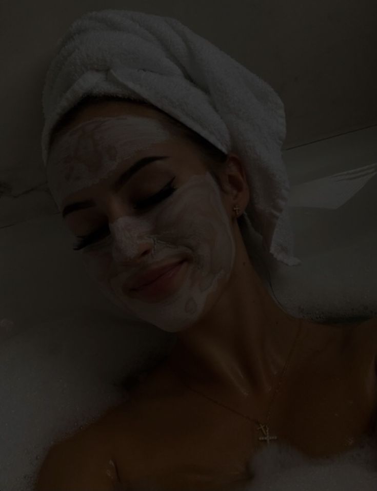 a woman with a towel on her head is in the bathtub and she's wearing a face mask