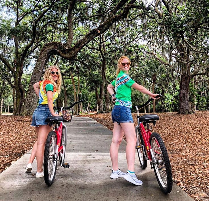 two young women standing next to each other on bikes in the middle of a park