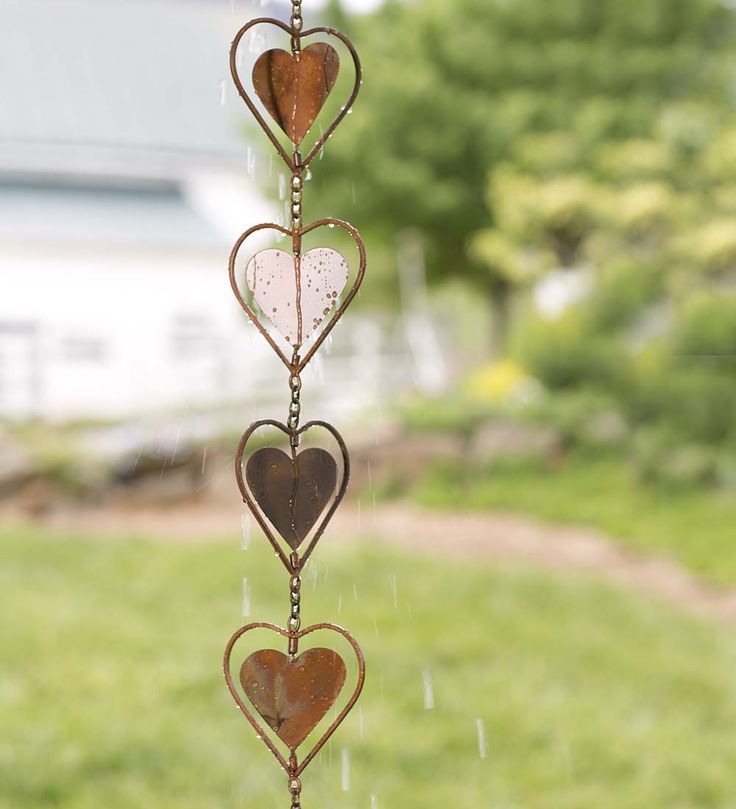 a wind chime with hearts hanging from it's sides in the grass near a house