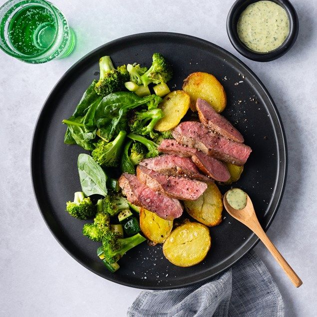 a black plate topped with meat, potatoes and broccoli