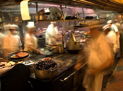 blurry image of chefs in a restaurant kitchen preparing food on pans and plates