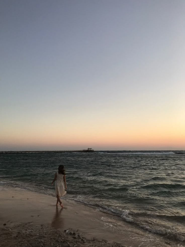 a woman walking along the beach at sunset