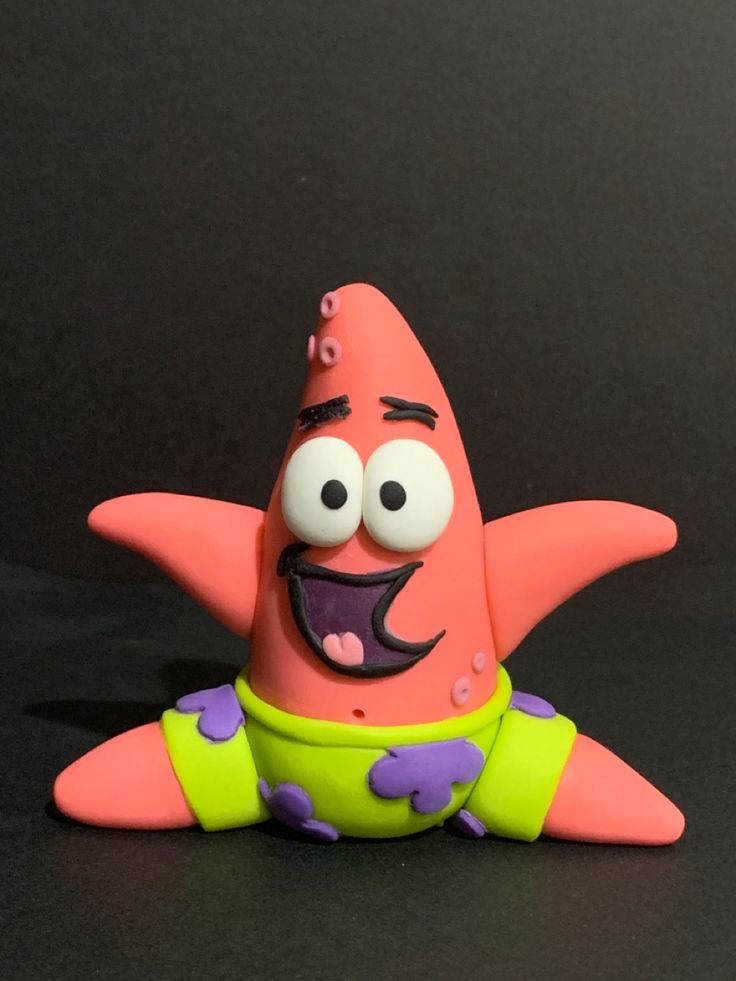 a pink toy with purple and green designs on it's body sitting in front of a black background